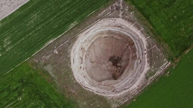 Top down drone footage inside a large dry sinkhole, showing steep eroded walls, cracked soil layers, geological textures, natural ground collapse, and karst terrain from above.