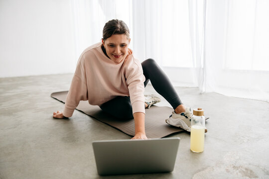 Woman using laptop for online fitness session on yoga mat at home