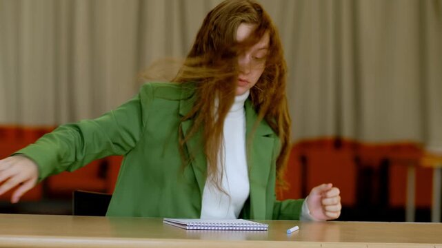Young woman in green suit angrily tearing assignment paper at classroom table, throwing away failed attempt, theme frustration burnout and perfectionism in student life.