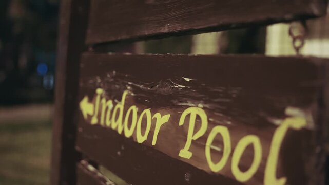 Wooden direction sign with the text Indoor Pool lit during the evening hours