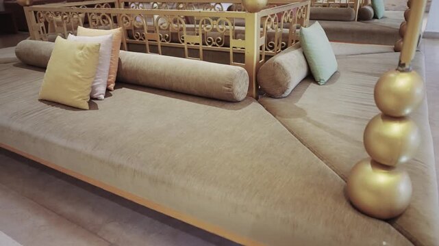 Luxurious seated arab style lounge featuring plush soft cushions in various pastel shades and intricate golden decor