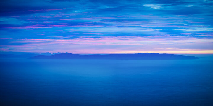 Aerial view of the Mull of Kintyre silhouette across the deep blue sea under a vibrant pink and blue twilight sky United Kingdom.
