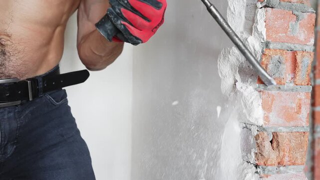 Close up of worker operating demolition tool on brick wall during interior renovation. Concept of demolition process and construction repair.
