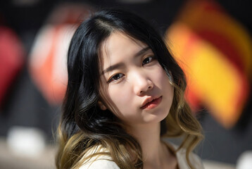 Fototapeta premium A young East Asian woman with long dark hair is posing for a portrait against a blurred, colorful background.