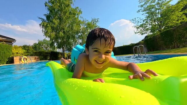 Happy young boy floating on an inflatable mattress in a swimming pool