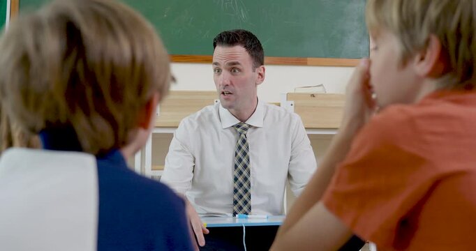 Close classroom circle view follows male adult teacher talking with young boy and girl pupil group, building listening skill, question time, routine, first day class engagement and respect today