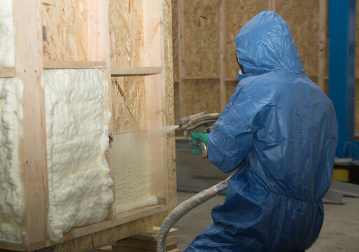 A construction worker in overalls applies insulation foam to a wooden wall of a house, house construction and insulation