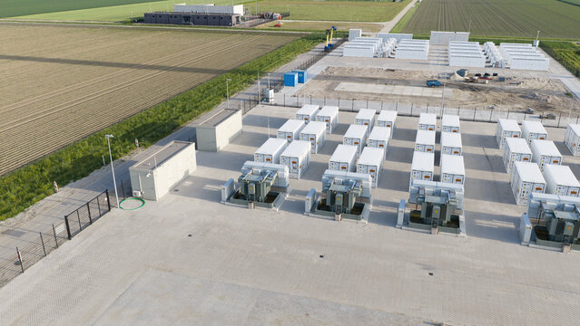 Aerial view of a large-scale battery energy storage system with white containers and electrical transformers near agricultural fields in Dronten, Flevoland, Netherlands.