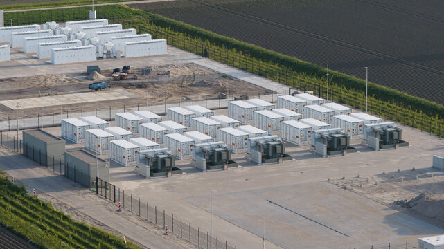 Aerial view of a large scale battery energy storage system with rows of white container units and electrical transformers located near agricultural fields Dronten, Flevoland, Netherlands.