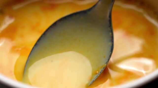 Metal spoon stirring bright orange turmeric powder into warm vegan rice drink to prepare a healing golden milk latte. Traditional ayurvedic wellness concept