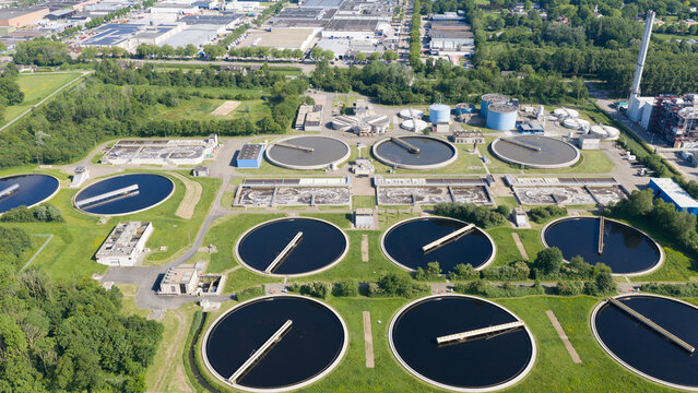 Aerial view of the Rwzi Weurt wastewater treatment plant featuring circular sedimentation tanks and industrial facilities surrounded by lush greenery in Weurt, Gelderland, Netherlands.