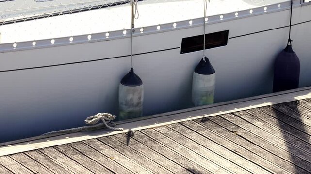 Side view of a white luxury yacht docked a weathered wooden deck pier with protective boat fenders. Summer vacation concept
