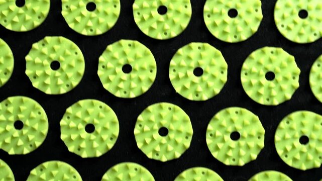 Close up texture of green acupressure massage mat elements arranged in a repeating geometric pattern on a black fabric background