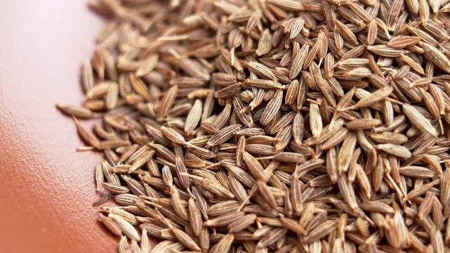 Whole cumin (jeera) seeds in brown bowl. Traditional herbal seasoning. Aromatic condiment. Top view. Rotation