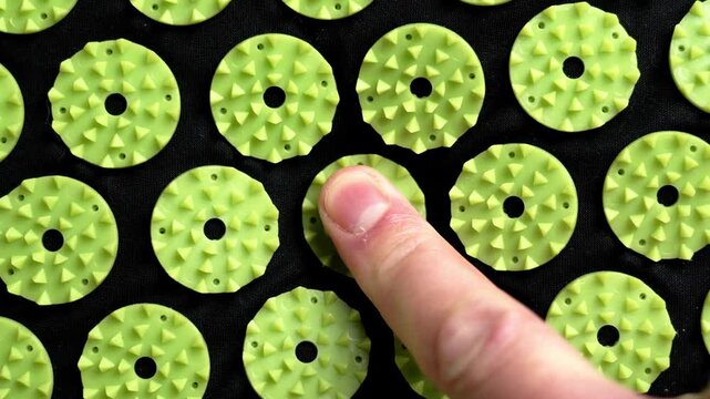 Human finger pressing acupressure spike on a therapeutic massage mat close up