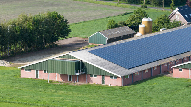 Aerial view of a large farm building with solar panels on the roof surrounded by green fields and silos in Giethoorn, Overijssel, Netherlands.