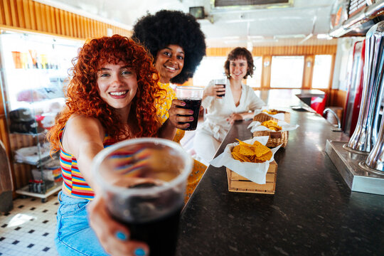 Multiethnic young women friends bonding at vintage diner counter - Happy multiracial students meeting in a fast food restaurant to have fun together and celebrate