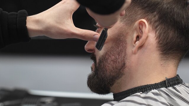 Professional barber performing precise beard shaving with classic straight razor, working in modern barbershop with skilled grooming technique