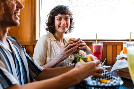 Happy friends enjoying burgers and smoothies at diner - Happy multiracial students meeting in a fast food restaurant to have fun together and celebrate