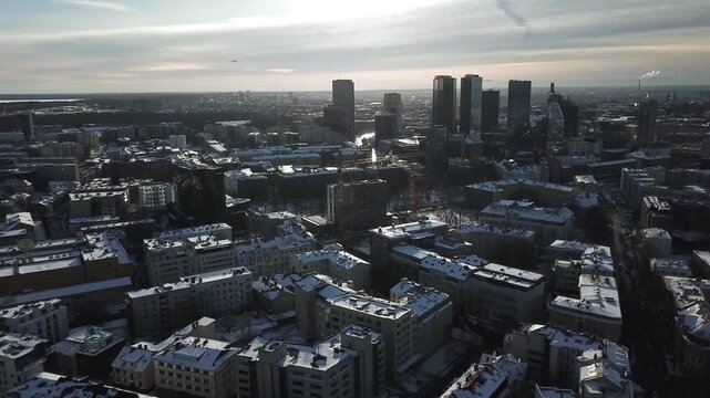 Aerial view of modern cityscape with skyscrapers and snow covered rooftops in winter afternoon light.