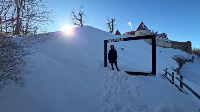 Person posing in a photo frame sculpture at Bauska Castle in Latvia winter snow covered landscape
