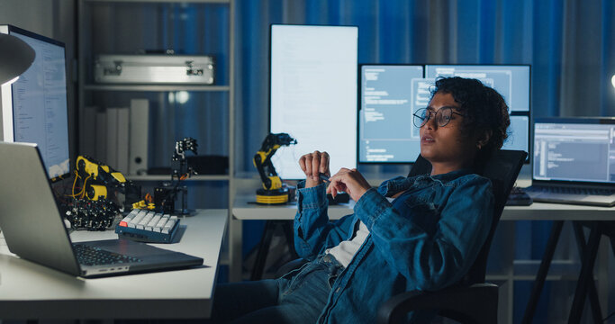 Young African American female programmer coding AI software on multiple screens in night office. Network security, cybersecurity, machine learning, working late, overtime, robotics automation concept.