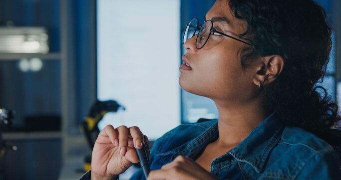 Close-up young Black female programmer coding AI software on multiple screens in night office. Network security, cybersecurity, machine learning, working late, overtime, robotics automation concept.