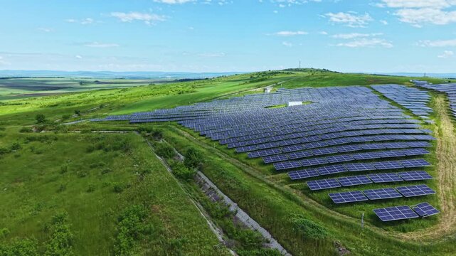 Rolling hill solar beds with grass, tight rows of panels following contour, access track, wildflower margins, blue sky, drone sweep, sustainable countryside
