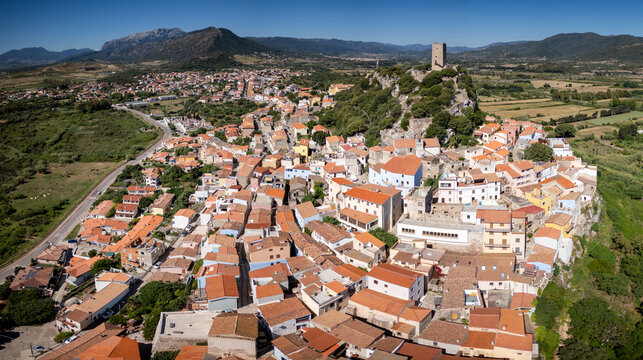 Aerial view of the historic town of Posada with the Castello della Fava tower on a rocky hill overlooking colorful rooftops and green landscapes Posada, Sardinia, Italy.