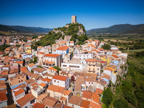 Aerial view of the historic Castello della Fava and the colorful rooftops of the old town under a clear blue sky in Posada, Sardinia, Italy.