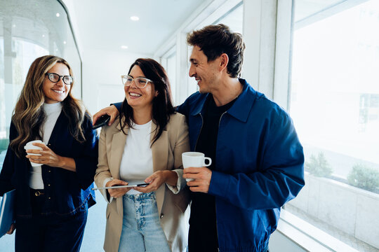 Three coworkers chat and drink coffee in hallway