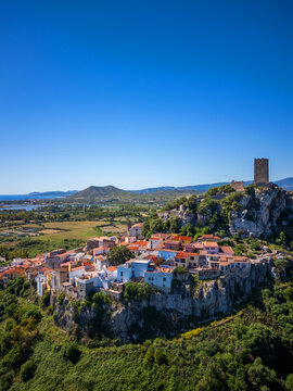 Aerial view of Castello della Fava and the historic center perched on a limestone cliff with colorful houses under a clear blue sky in Posada, Sardinia, Italy.
