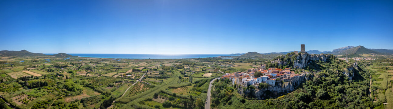 Aerial view of the historic Castello della Fava and the medieval town of Posada perched on a rocky hill overlooking the green valley and the sea Posada, Sardinia, Italy.