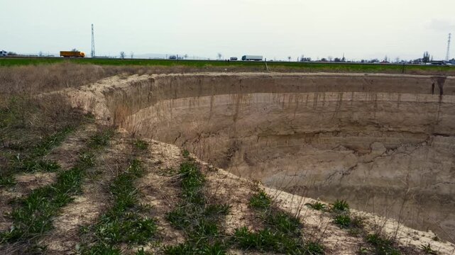 Ground-level footage showing a large sinkhole with steep eroded walls in a rural landscape. Geological formation, natural ground collapse, karst terrain, and dry soil textures are clearly visible.