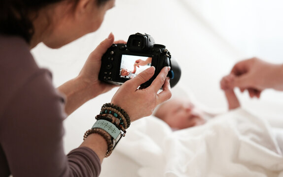 Woman Takes Pictures Of Newborn Baby While Mom Holds Baby Hand. Bright And Warm Setting.