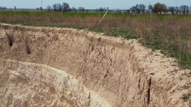 Ground-level footage showing a large sinkhole with steep eroded walls in a rural landscape. Geological formation, natural ground collapse, karst terrain, and dry soil textures are clearly visible.