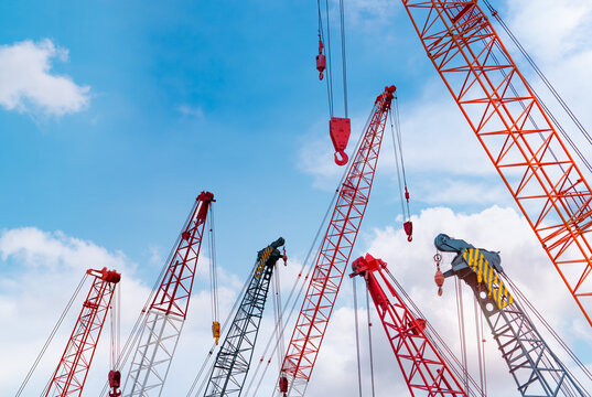 Crawler crane against blue sky and white clouds. Real estate industry. Red crawler crane use reel lift up equipment in construction site. Crane for rent. Crane dealership for construction business.