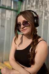 Fototapeta premium Woman enjoying a sunny day with headphones, sunglasses, and a playful spirit in a vibrant outdoor setting