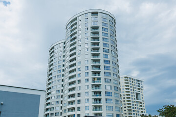 Fototapeta premium Tall residential buildings stand under a cloudy sky in a city as people walk on the street below during the day
