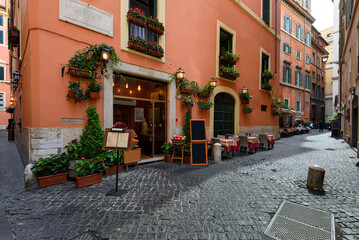 Obraz premium View of old narrow street with tables of restaurant in Rome, Italy. Architecture and landmark of Rome. Cozy cityscape of Rome.