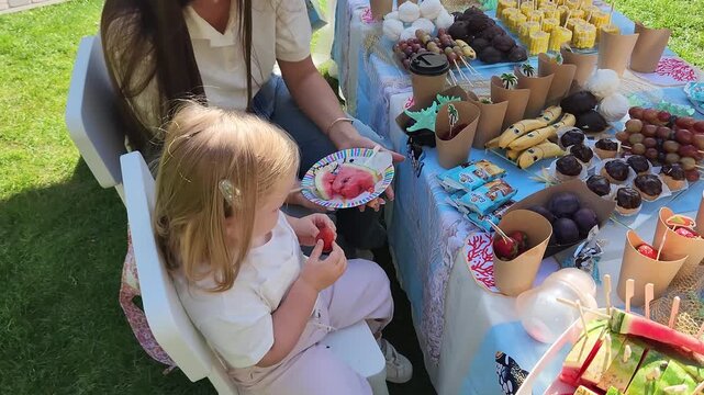 Little blonde girl eating snacks at a decorated festive table