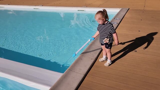 Toddler girl Sofia dipping a long skimmer net into a swimming pool