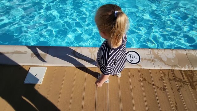 Top view of little Sofia standing on a wooden deck near a pool sign