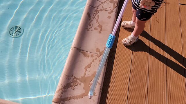 Close-up of a long-handled brush cleaning the pool border