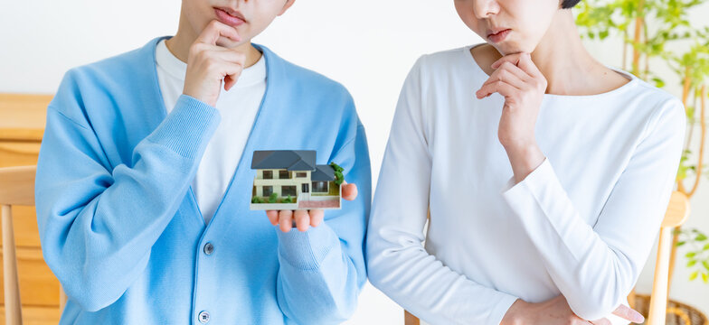 日本人カップルが家の模型を持って住宅購入を悩むシーン