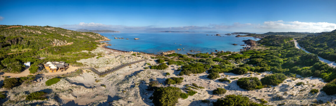 Aerial view of Bassa Trinita Beach featuring turquoise waters, white sand dunes, and lush Mediterranean vegetation in La Maddalena, Sardinia, Italy.