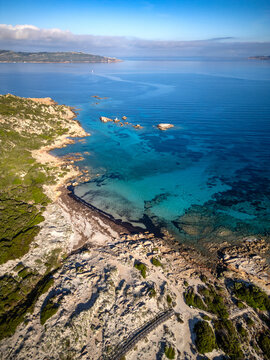 Aerial view of Bassa Trinita Beach featuring crystal clear turquoise waters, rugged rocky coastline, and lush Mediterranean scrub La Maddalena, Sardinia, Italy.