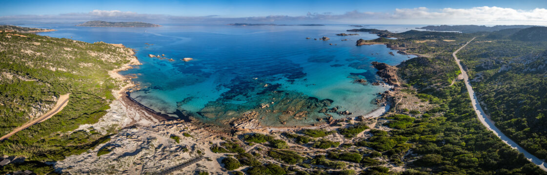Aerial view of Bassa Trinita Beach with turquoise waters, granite rocks, and lush Mediterranean vegetation, La Maddalena, Sardinia, Italy.