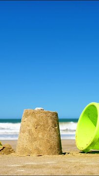 sandcastle on a sandy beach with a green bucket near the sea
