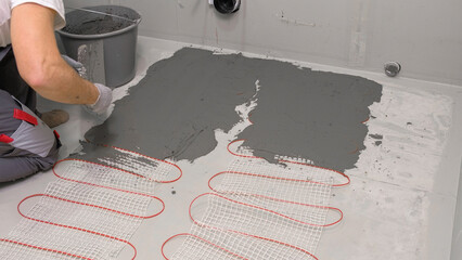 Fototapeta na wymiar Electric Heating Mat Installing in the Tile Adhesive. Underfloor Dual Core Fiberglass Mesh Mat. Warm Floor Heating System. Warming. Worker Applying Concrete Mortar for Warm Floor. Renovation work. 4K